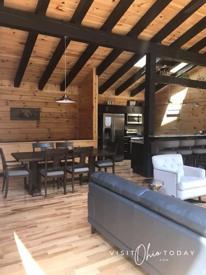 inside of cabin with beams on ceiling, leather chair and wooden table with 6 chairs