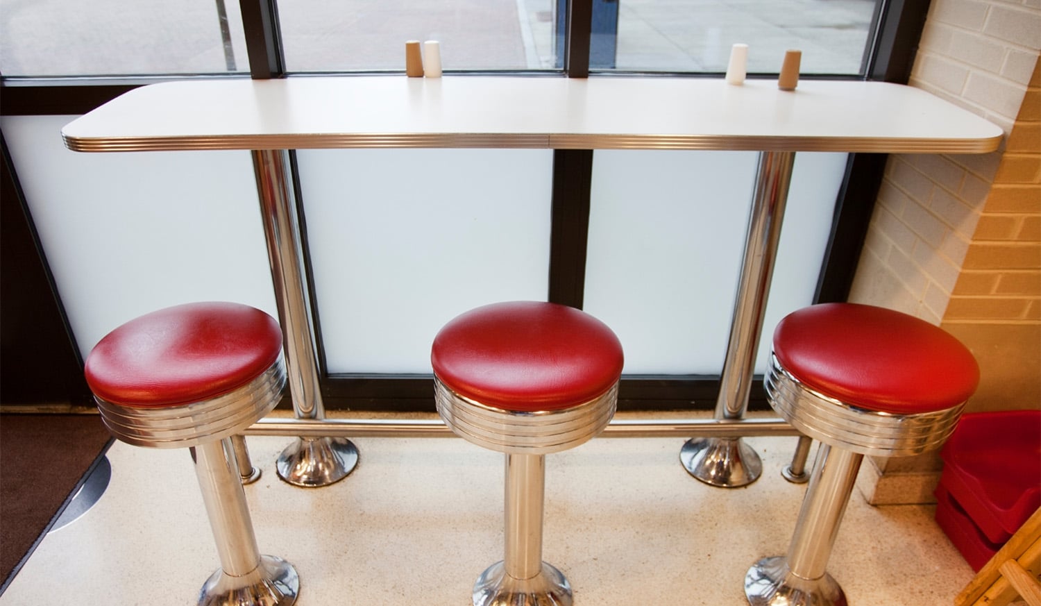 horizontal photo of three diner stools by a bar table in front of a window with a wooden floor. Image via Canva pro license