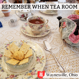 square image of a photo of a cheeseball and crackers at Remember When Tea Room. There is a teapot and a cup of tea on a table with a lace cloth. A white strip at the top has the text Remember When Tea Room