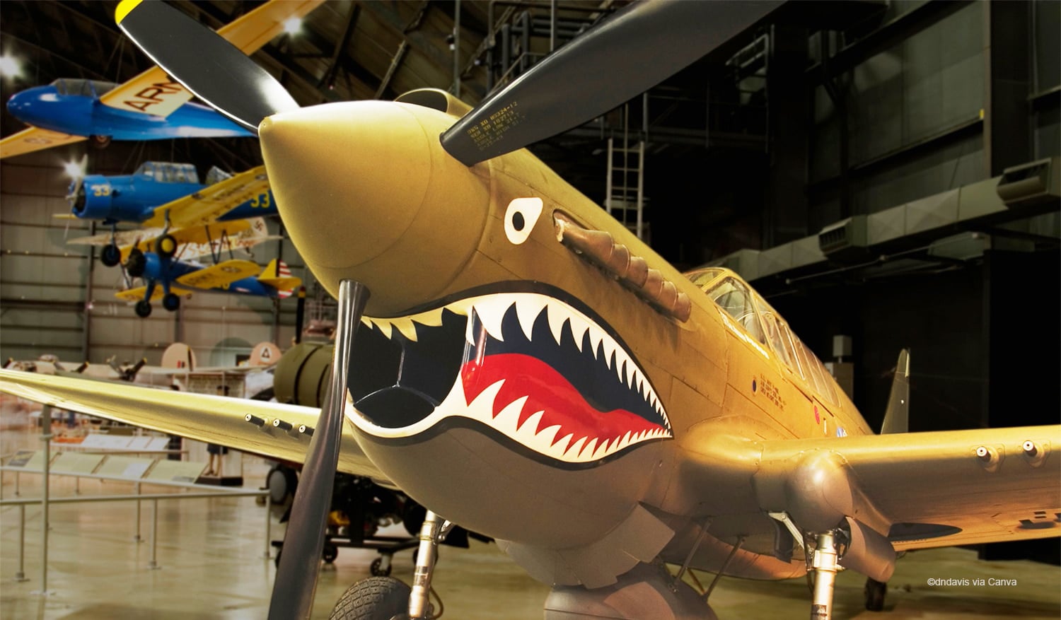 horizontal photo of a yellow airplane with a painted on shark mouth at the National Museum of the US Air Force. Image via Canva pro license