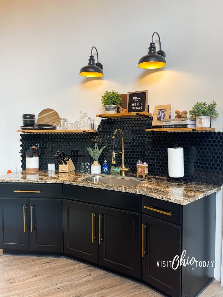 pictured is a portion of the kitchen in the silo cottage in hocking hills, there are black cabinets with a stink and bowls and plates on a shelf