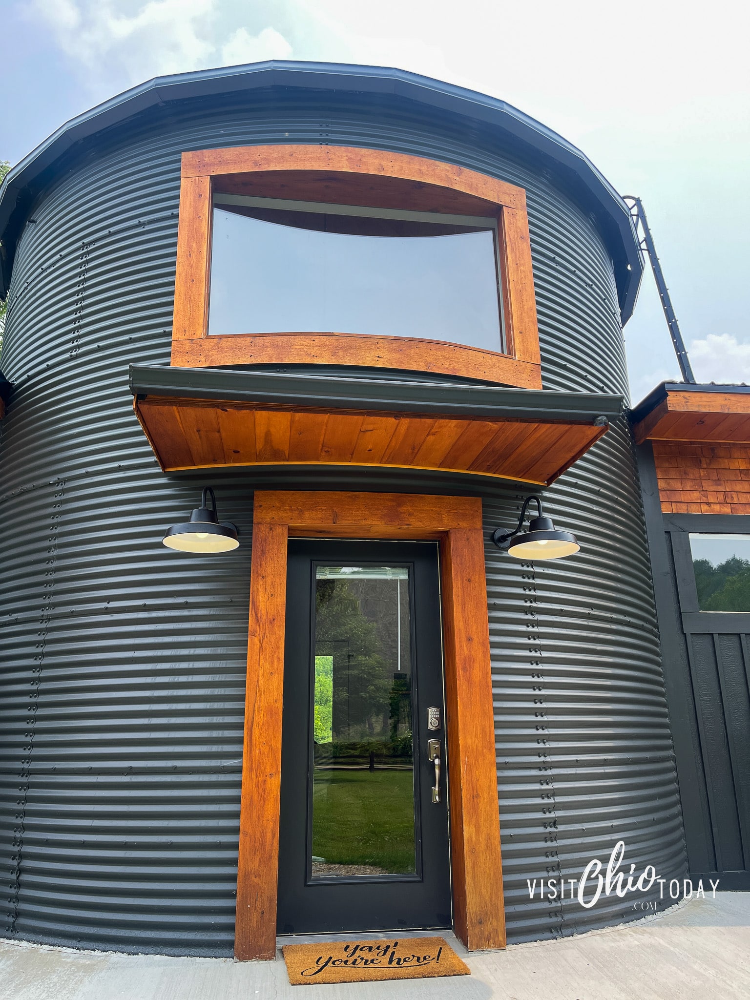 close up of the silo portion of the silo cottage in hocking hills, you can see the front door with has dark wood around it and a large window above the door with wood around it. Photo credit: Cindy Gordon of VisitOhioToday.com