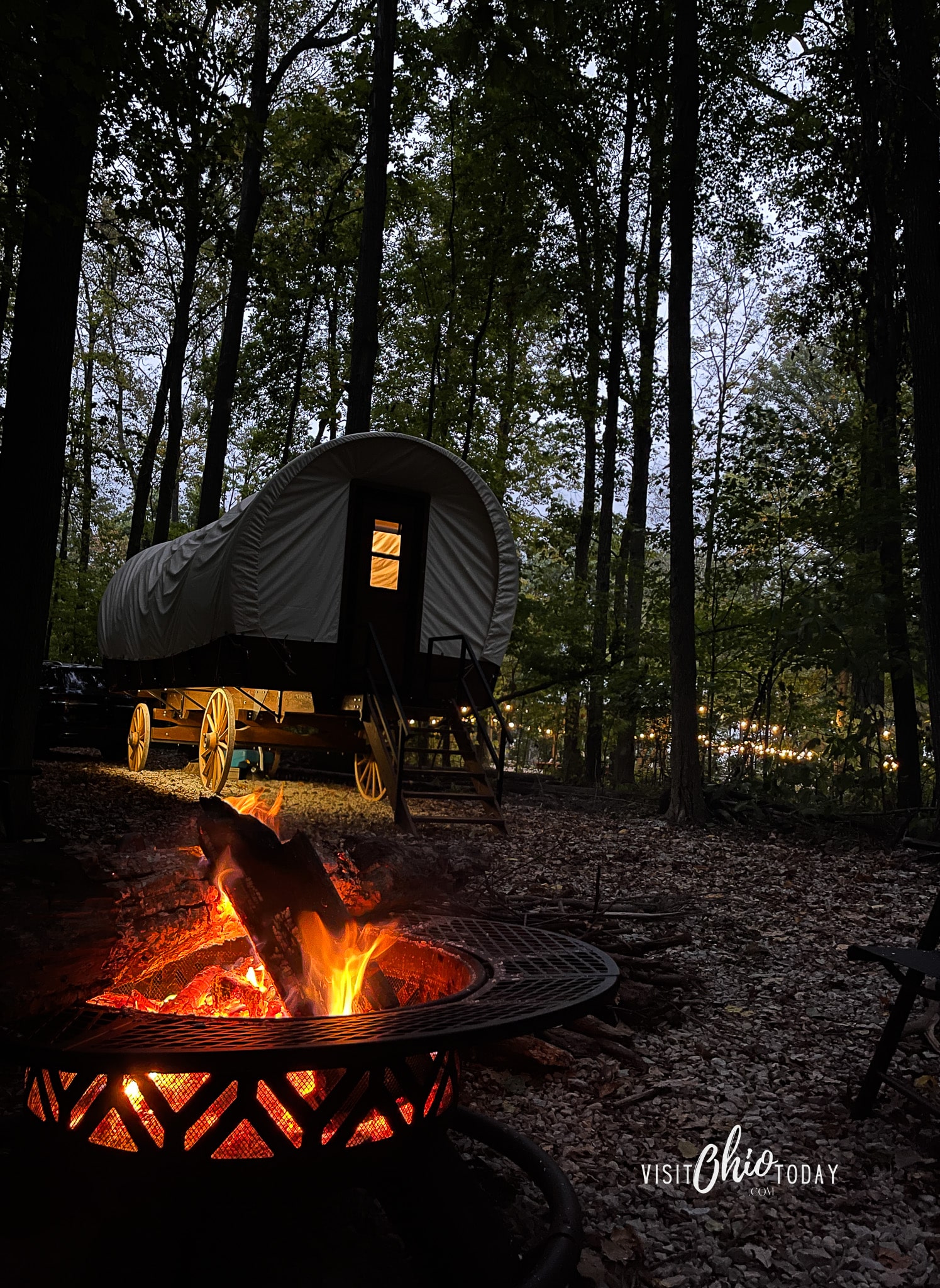 picture of the lux covered wagon at graystone ranch at night. There is a fire in the front of the phtos and a covered in the back. There is a light on inside and under the wagon. The sky is dark Photo credit: Cindy Gordon of VisitOhioToday.com