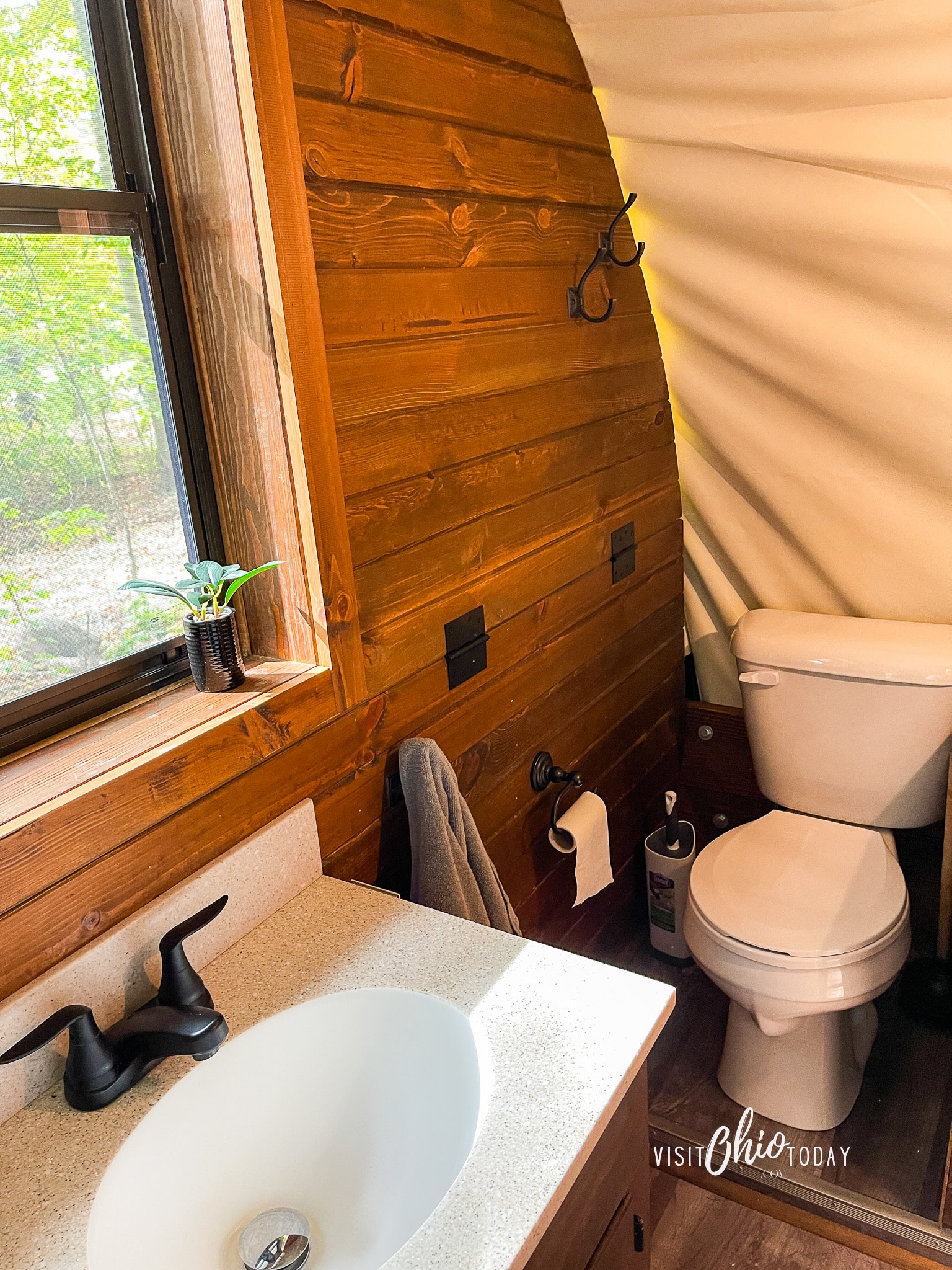 photos from inside the lux covered wagon at garystone ranch, a full working bathrooms, pictured a sink, window to outside where you can green tree leaves and a toilet Photo credit: Cindy Gordon of VisitOhioToday.com