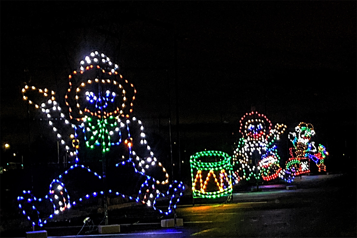 horizontal photo of some lit-up characters and drum along a drive through Christmas lights route