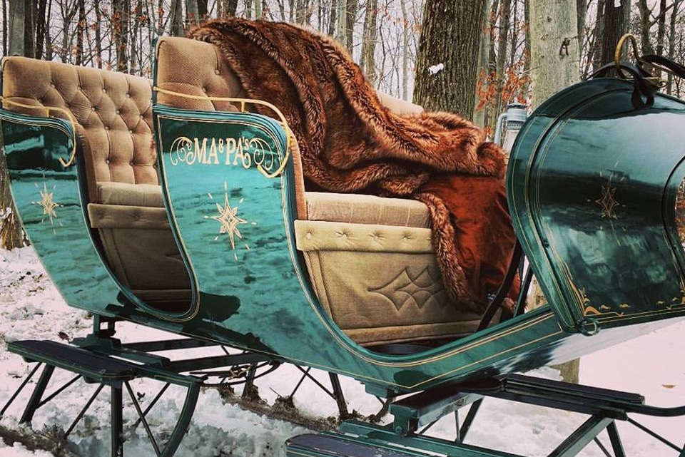 horizontal photo of a green sleigh with tan colored padded seats and a brown furry blanket