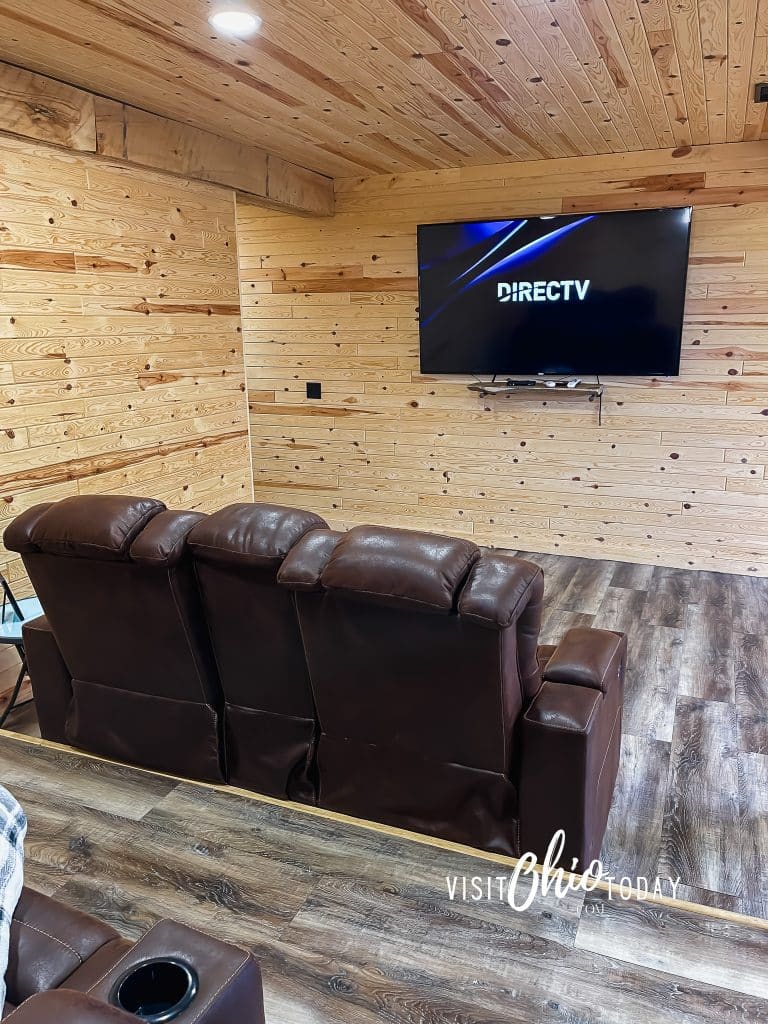 downstairs theater room in woodlands lodge, you can see back of leather chairs and tv on wooden paneled wall Photo Credit Cindy Gordon of VisitOhioToday.com
