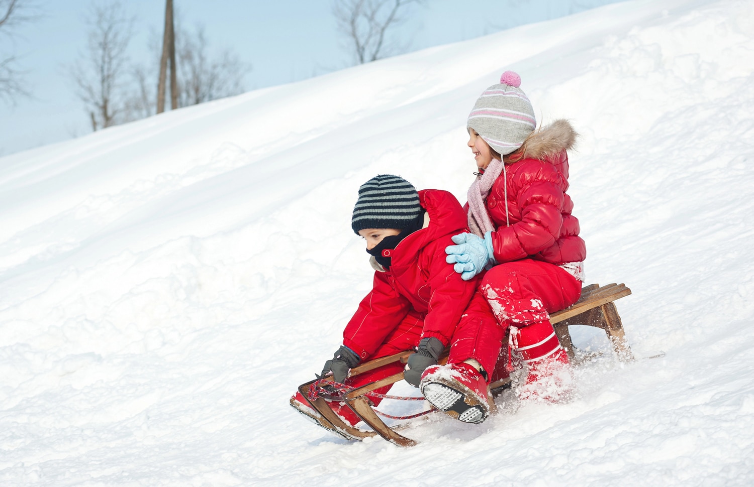 horizontal photo of two children dressed in red coats on a sled