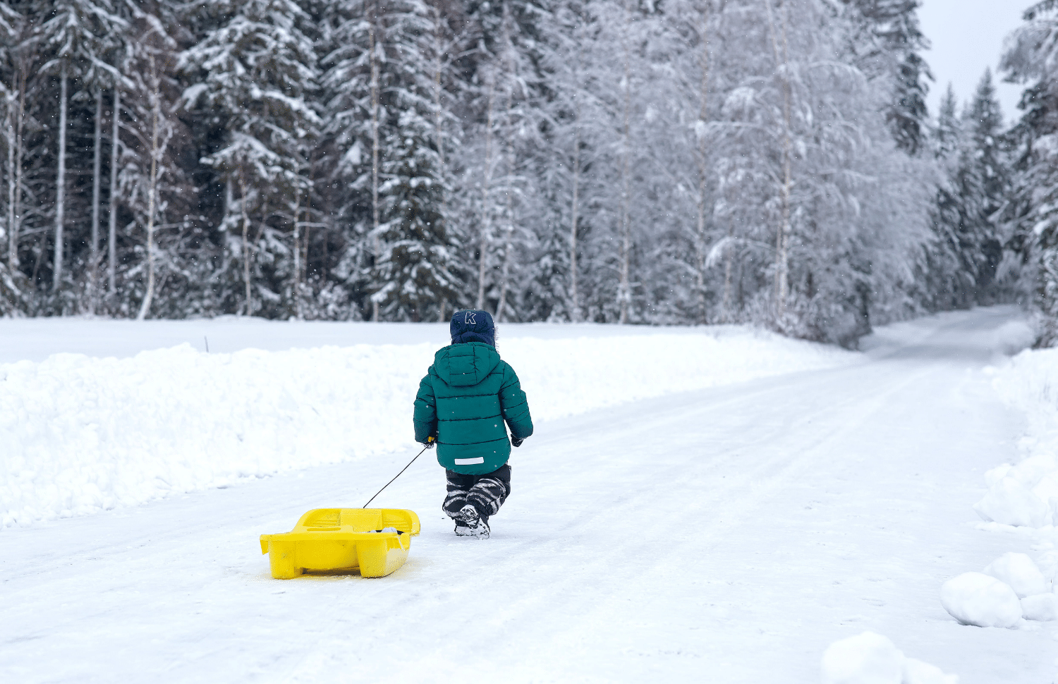 horizontal photo of a young child pulling a sled up a snowy hill