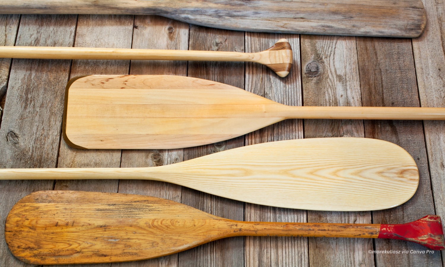 horizontal photo of canoe paddles arranged on a wooden surface