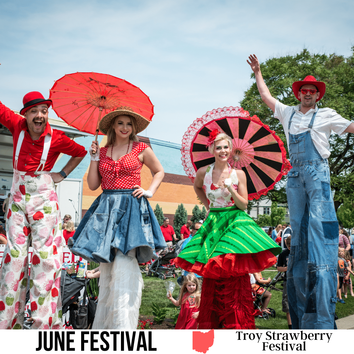 A square image of a photo of two men and two women dressed in strawberry-themed clothing, on stilts. The women are holding parasols. A white strip across the bottom has text June Festival Troy Strawberry Festival.