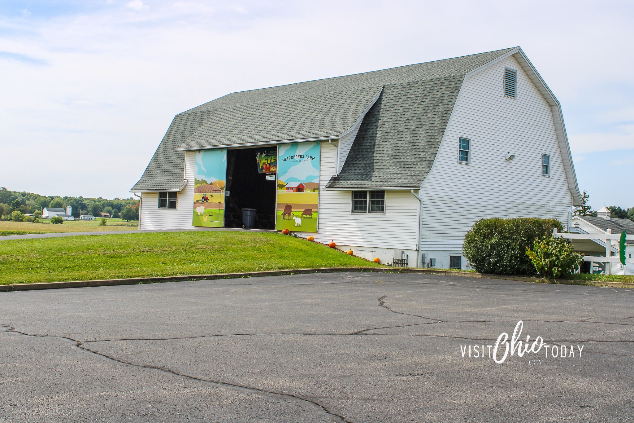 horizontal photo of a photo of a white barn with grass in front and a parking lot in the foreground. Photo credit: Cindy Gordon of VisitOhioToday.com