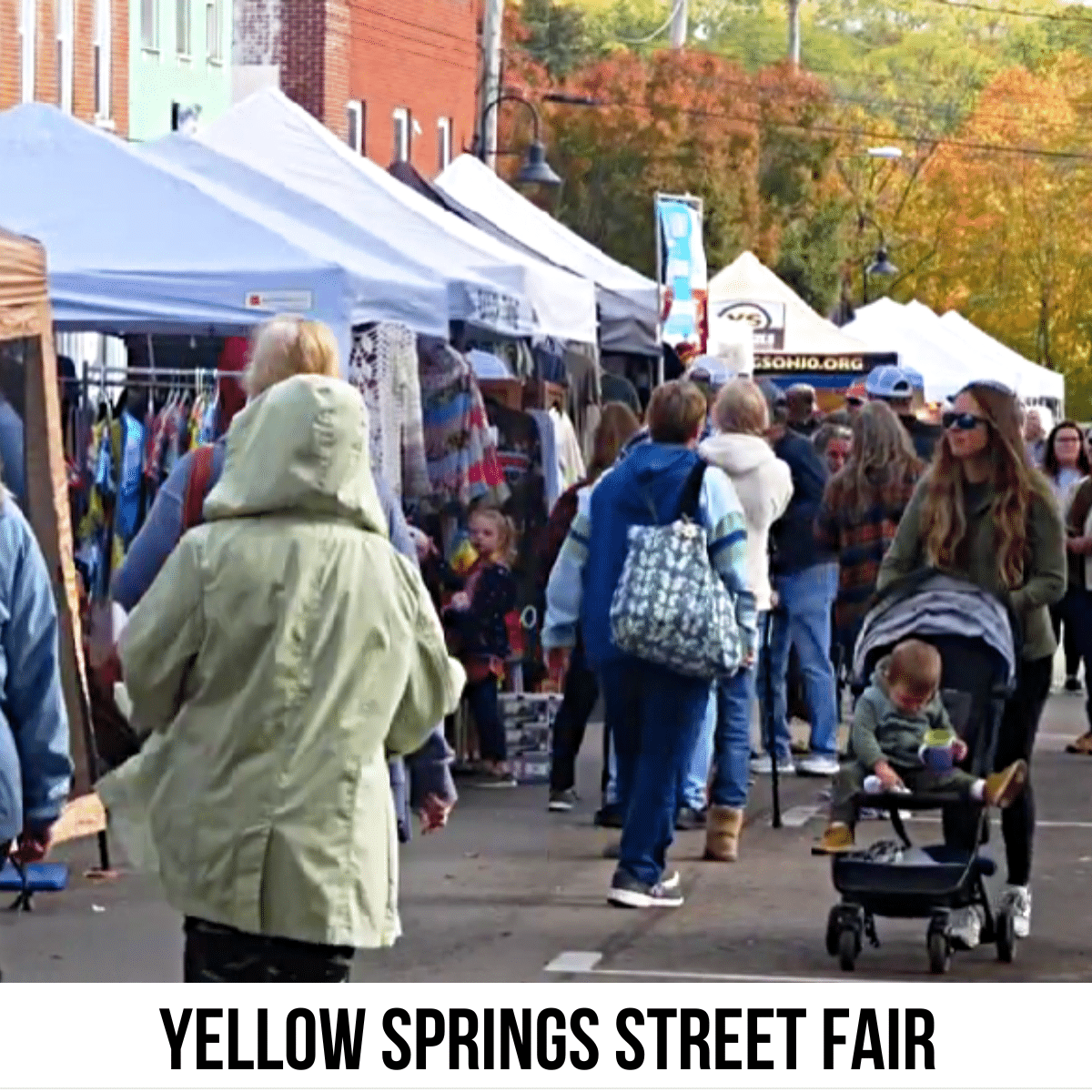 A square image of people at a street fair. The street is lined with white tents selling goods. A white strip across the bottom has text Yellow Springs Street Fair