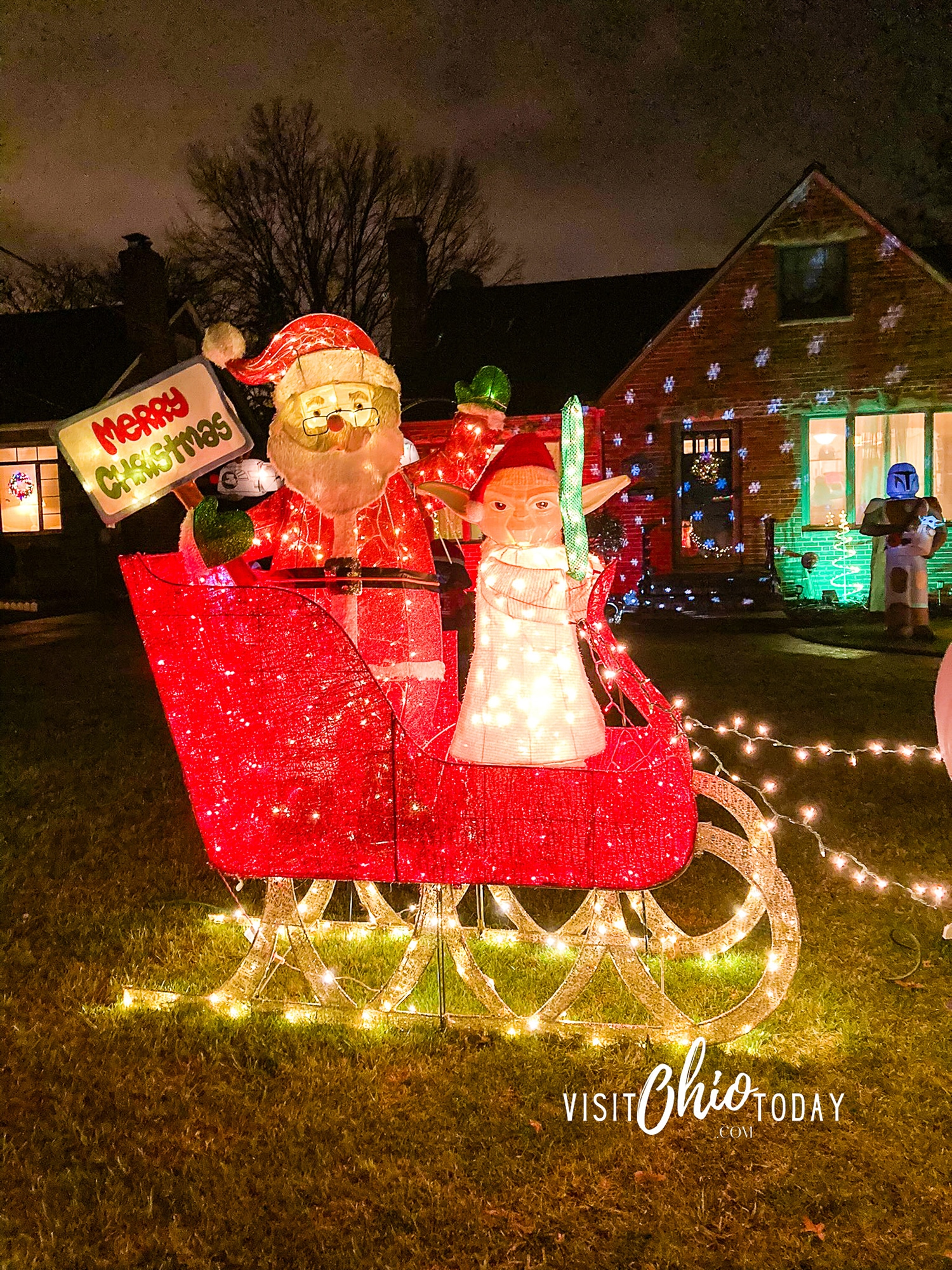 vertical photo of a Christmas display at Fairview Park Holiday Lights with Santa holding a merry Christmas sign and a Star Wars Elf character holding a light saber. Photo credit: Cindy Gordon of VisitOhioToday.com