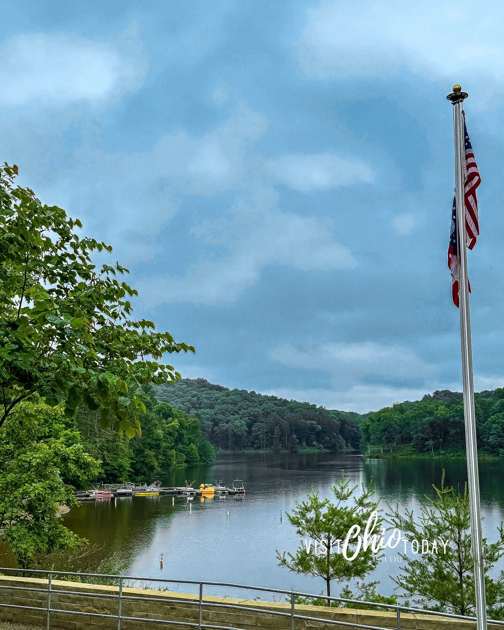 vertical photo of Lake Hope with some moored boats. Trees line the sides and background of the photo and an Ohio flag is in the foreground. Photo credit: Cindy Gordon of VisitOhioToday.com