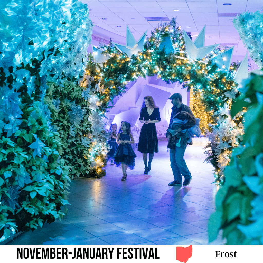 A square image of a photo of a man, a woman, and two young children walking through frosted decorated walkway, with white poinsettas and blue and white lighting. A white strip across the bottom has text November-January Festival Frost.