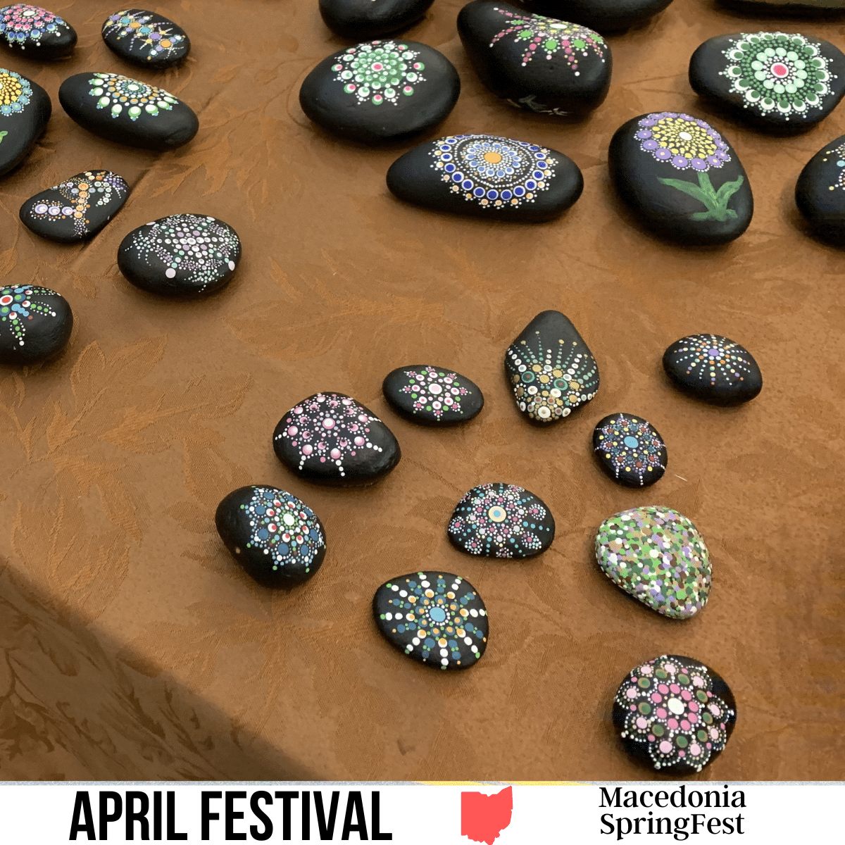 square image with a photo of painted stones at a craft fair. A white strip across the bottom has the text April Festival. Macedonia SpringFest