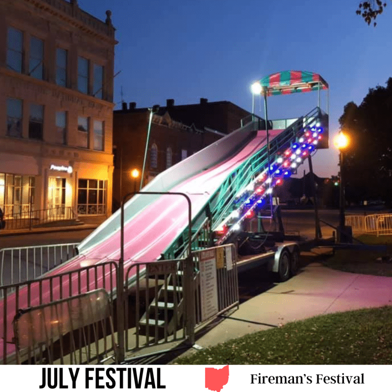 square image with a photo of a lit slide at a fairground. A white strip across the bottom has the text July Festival. Fireman's Festival