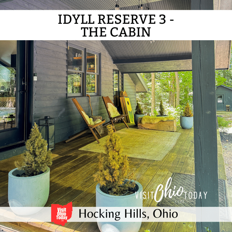 square image with a photo of the outside deck area at The Cabin. A white strip across the top contains the text Idyll Reserve 3 - The Cabin, and a white strip across the bottom has the text Hocking Hills, Ohio