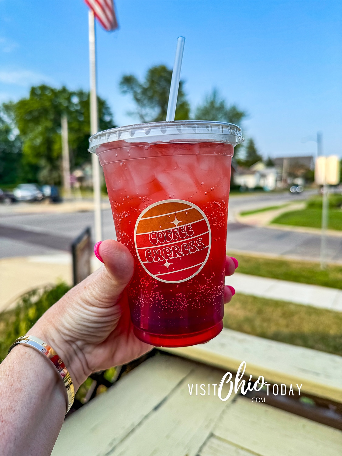 vertical photo of a hand holding a cup of red drink with the Coffee Express logo and the street in the background. Photo credit: Cindy Gordon of VisitOhioToday.com
